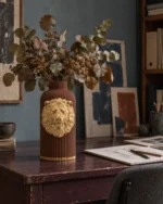 Vaso Leone Potente marrone con decorazione color oro, ambientato con una composizione di rami secchi.