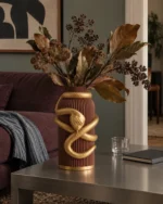 Vaso Serpente Avvolgente marrone con decorazione color oro, ambientato con una composizione di rami secchi.